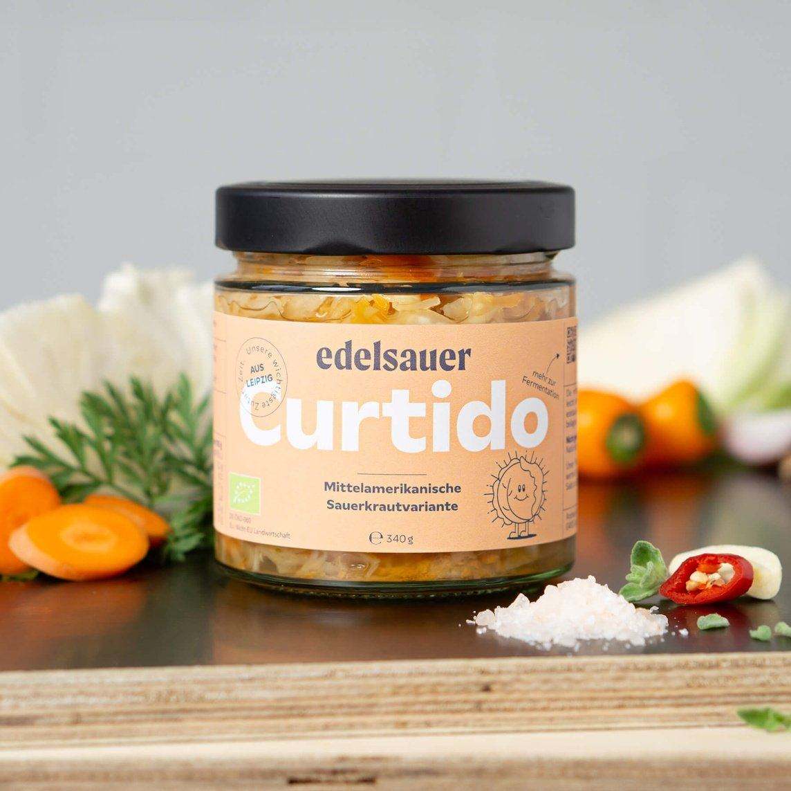 bio curtido von edelsauer im glas auf einer küchenplatte neben geschnittenem gemüse