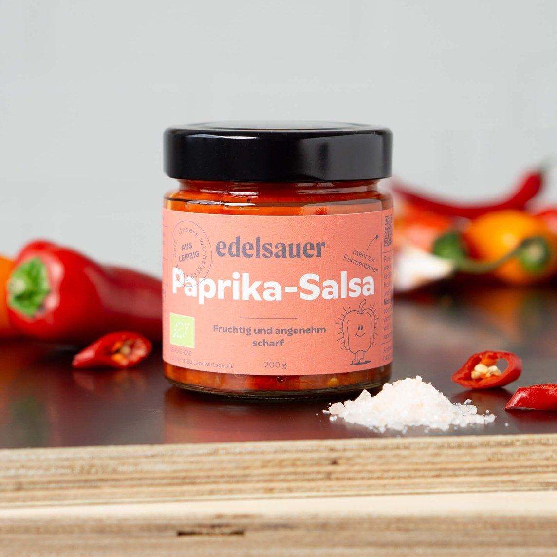 bio paprika salsa im glas auf einer küchen arbeitsplatte neben roten paprikas und chilli schoten