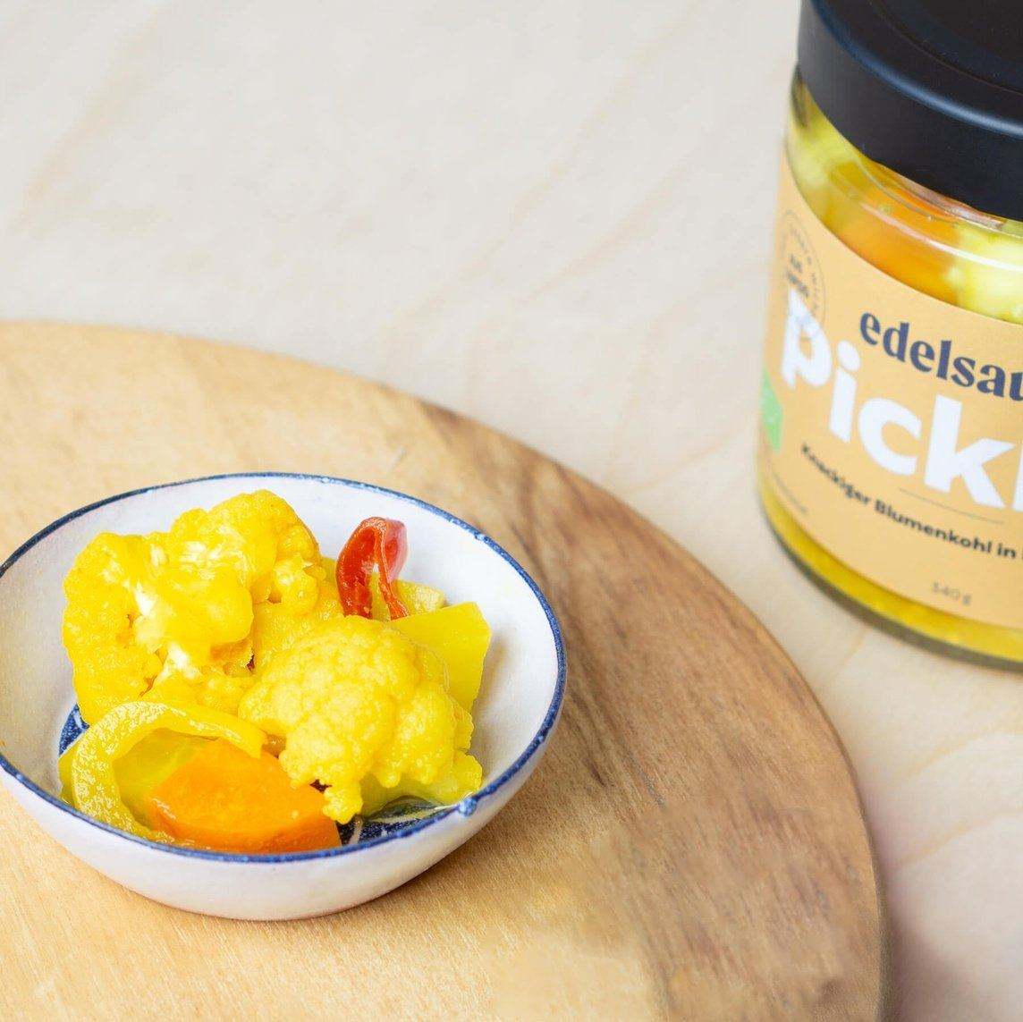Blumenkohl Pickles in einer weißen Schale auf einem Holz Brettchen und Glas mit edelsauer Pickels daneben
